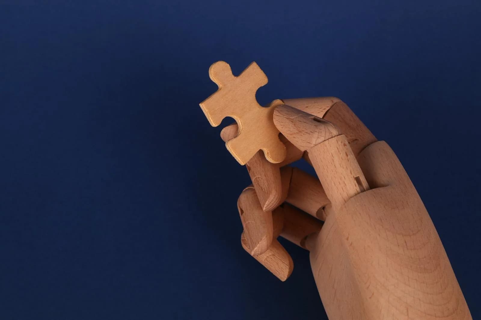 Pièce de puzzle tenue par une main en bois — symbole de la pièce manquante.